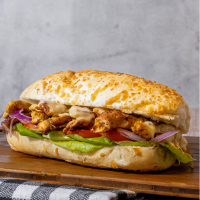 Pão baguete coberto de parmesão, filé de frango, queijo cheddar, cebola roxa e salada