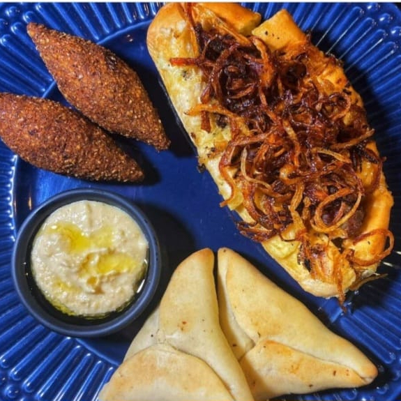 Pão de alho com kafta, cebola caramelizada, homus de 60g, 2 mini kibe de carne e 2 mini esfihas de carne.