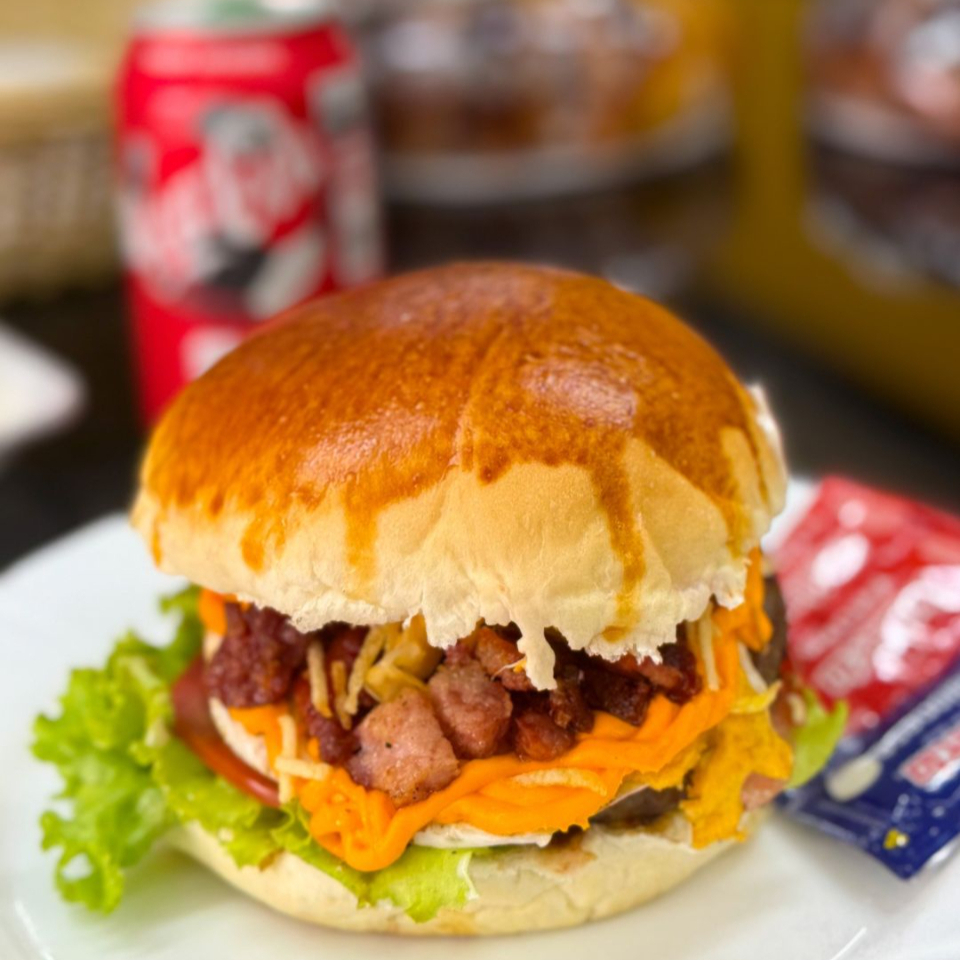 Um verdadeiro clássico! Hambúrguer de 120g com ovo, bacon crocante, muçarela, cheddar cremoso, maionese e finalizado com milho, batata palha, alface e tomate.