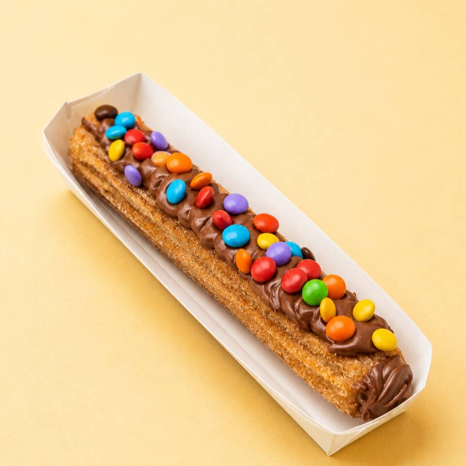 Churros crocante, macio por dentro e bem recheado, finalizado com cobertura cremosa e pedacinhos coloridos de M&M’s. Um clássico divertido e delicioso!