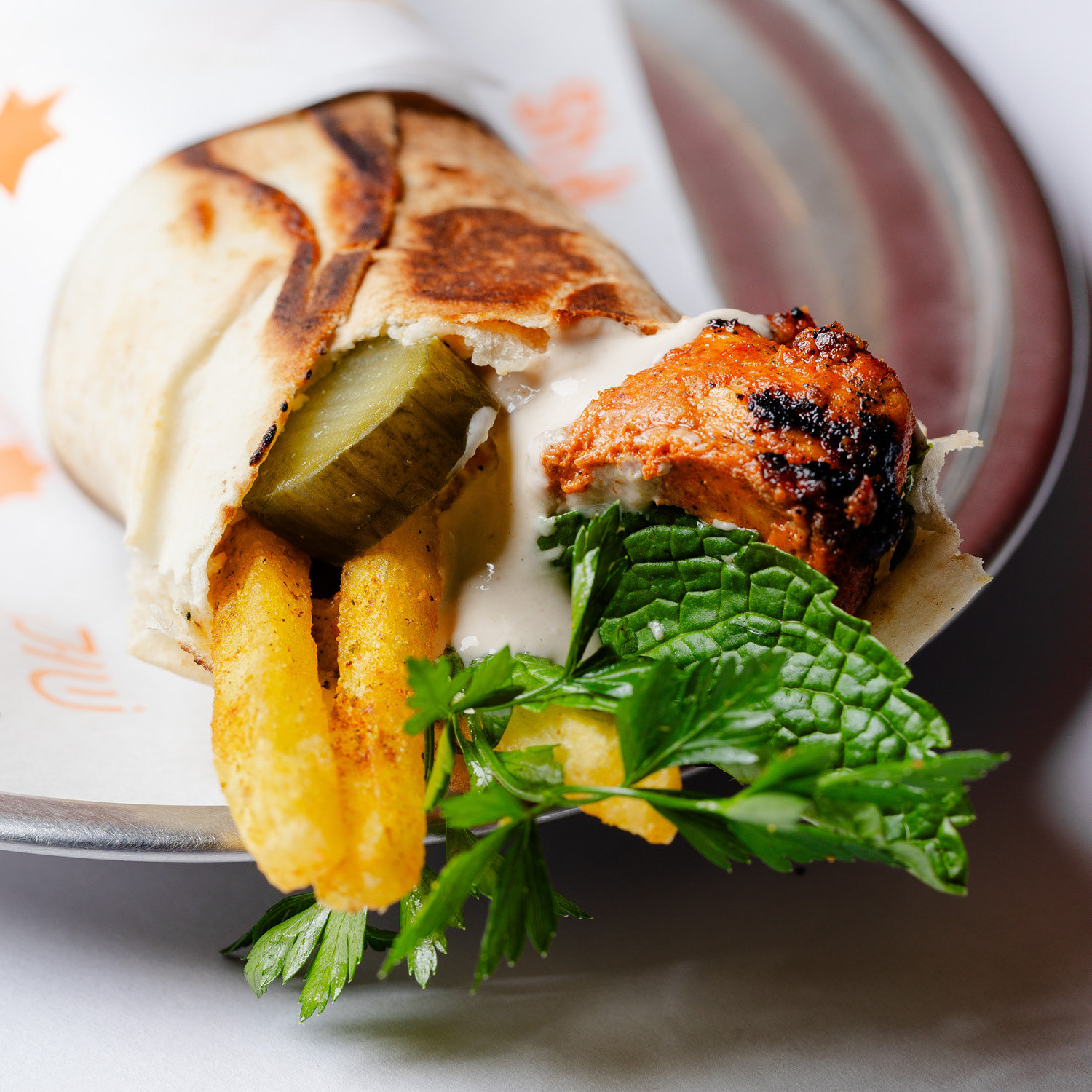 SANDUÍCHE ÁRABE DE FRANGO MARINADO EM PIMENTA HARISSA (PASTA MAGREBINA LEVEMENTE PICANTE DE PIMENTÃO VERMELHO E PIMENTAS), PASTA DE ALHO, FRITAS (DENTRO DO LANCHE), SALSINHA FRESCA, VINAGRETE (TOMATE, CEBOLA E MELAÇO DE ROMÃ) E MOLHO TAHINE, ENROLADO NO PÃO SÍRIO E PRENSADO. CONTÉM GLÚTEN. CONTÉM LACTOSE. CONTÉM OLEAGINOSAS.