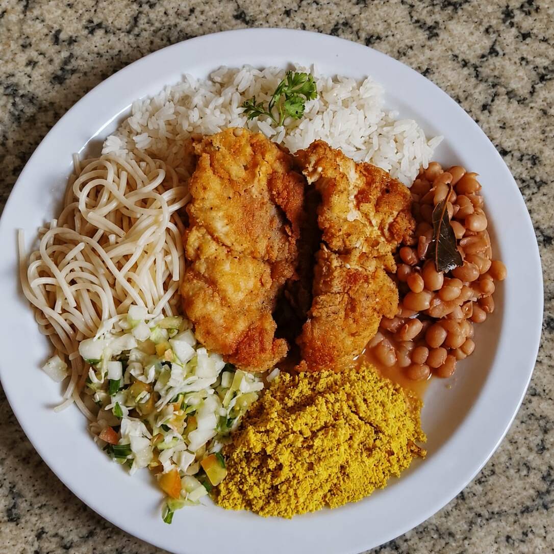 Frango empanado crocante e dourado, com arroz, feijão, farofa, salada e macarrão.