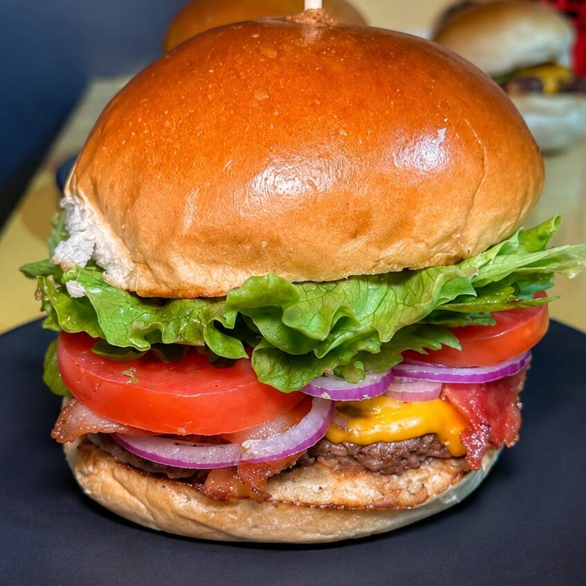 Clássico da Casa com ele não tem erro. Pão de brioche artesanal macio selado na Manteiga recebendo um hambúrguer especial 120g, queijo prato derretido, bacon premium crocante, cebola roxa, tomate e alface fresquinhos. Cortesia da Casa: Batata Rústica e+ a Super Maionese Temperada que é de tirar o fôlego.