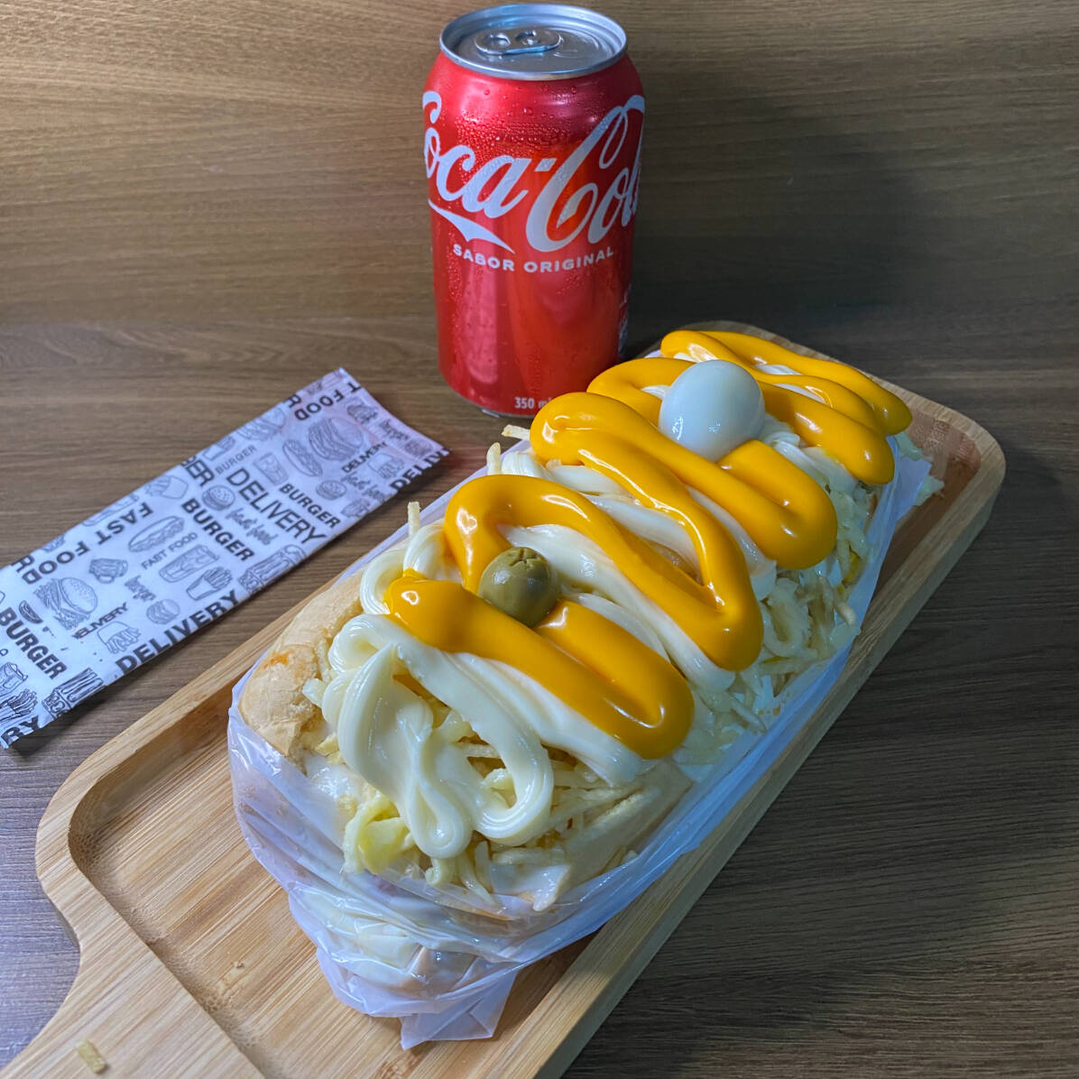 Acompanha: Pão, Salsicha ou Linguiça, Molho, Milho, Ervilha, Molho da Casa, Batata Palha, Queijo Mussarela Gratinado, Cheddar, Catupiry e Ovo de Codorna. *Coca-cola lata da imagem não inclusa. Pedir separadamente na categoria "bebidas".