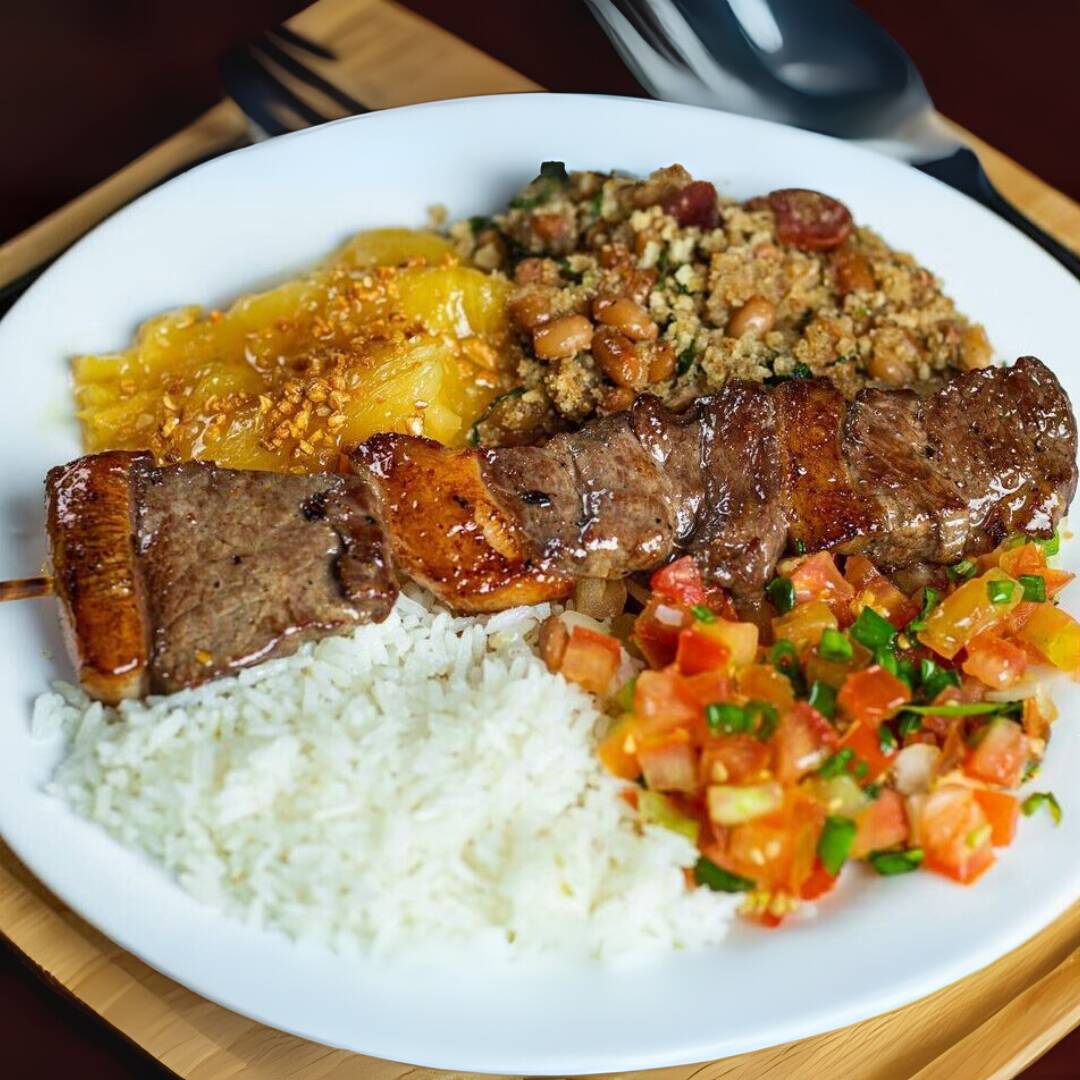 Espetinho de contra filé assado na brasa, arroz soltinho, feijão tropeiro com banana frita, mandioca cozida e vinagrete fresco. Marmitex completa e saborosa, ideal para o almoço. Serve 1 pessoa – Aproximadamente 650g.