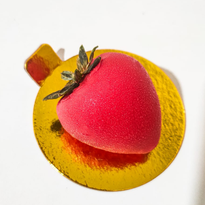 Isso não é um morango! É o nosso entremet Fraíse, é feito em formato de um morango, cheio de sabor, muito chocolatudo combinado com a acidez das frutas. Sendo feito com uma ganache de chocolate branco, recheado com ccremosa de morango, revestido com uma finíssima casquinha de chocolate. Cheio de texturas e sabores.