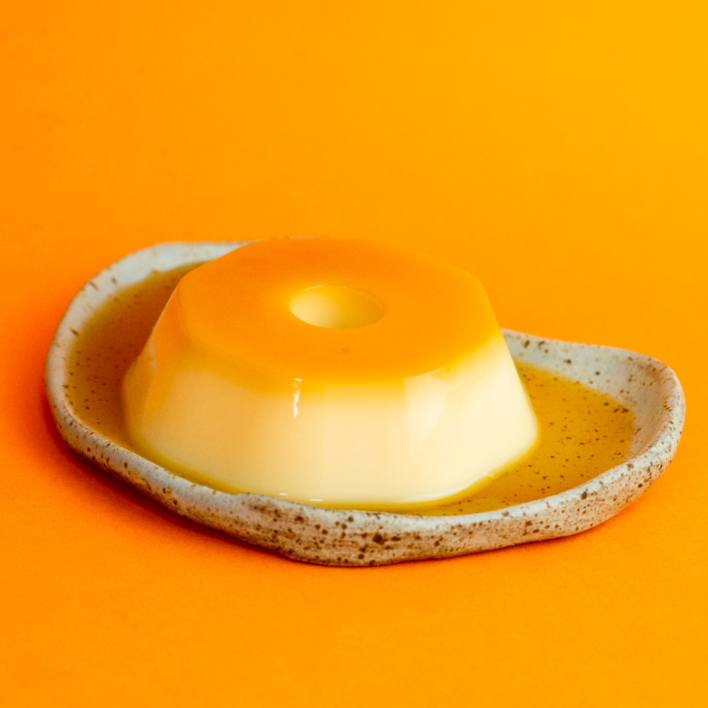 É uma sobremesa cremosa, com uma tonalidade levemente amarelada e uma calda de caramelo que adiciona sabor.