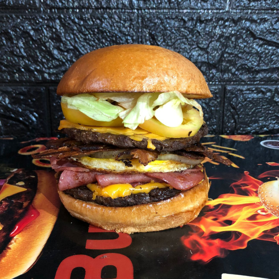 Pão brioche selado na chapa, duas carne bovina de 100g preparada na grelha, bacon, calabresa, presunto, ovo, queijo cheddar fatiado, picles, alface americana, tomate, cebola caramelizada e molho opcional.