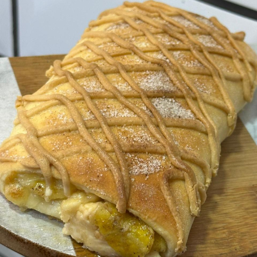 Joelho de massa macia e dourada, recheado com banana, chocolate branco cremoso e muçarela, finalizado com cobertura de chocolate branco e um toque de açúcar com canela.