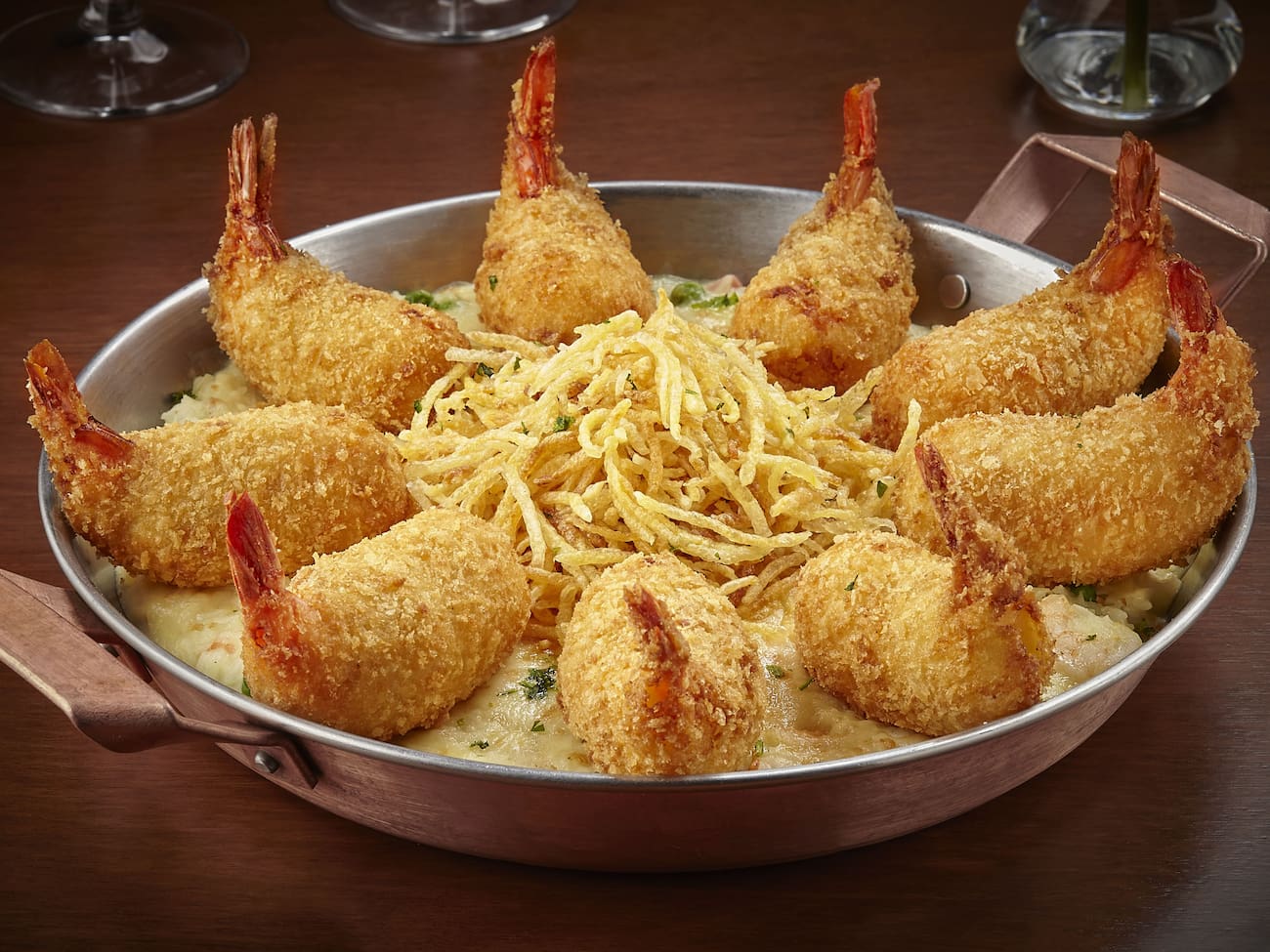 9 camarões empanados, recheados com queijo Catupiry, servido sobre cremoso arroz com camarão, ervilhas e presunto envolvido com molho branco. Gratinado com queijo mussarela. Acompanha batata palha.