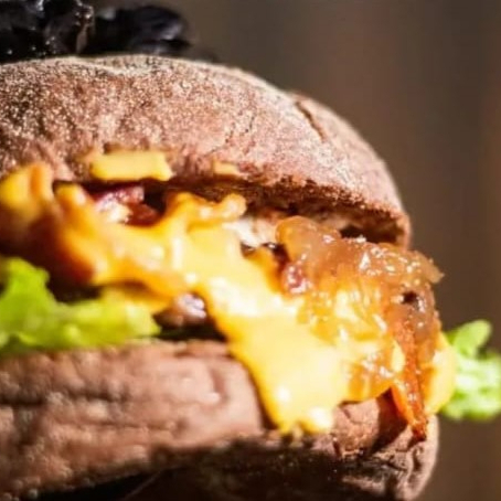 O Pão Americano macio da maná selado na manteiga com hamburguer de 100g , alface fresquinho americana , bacon crocante , queijo cheddar derretido e molho especial da casa entrega gratis
