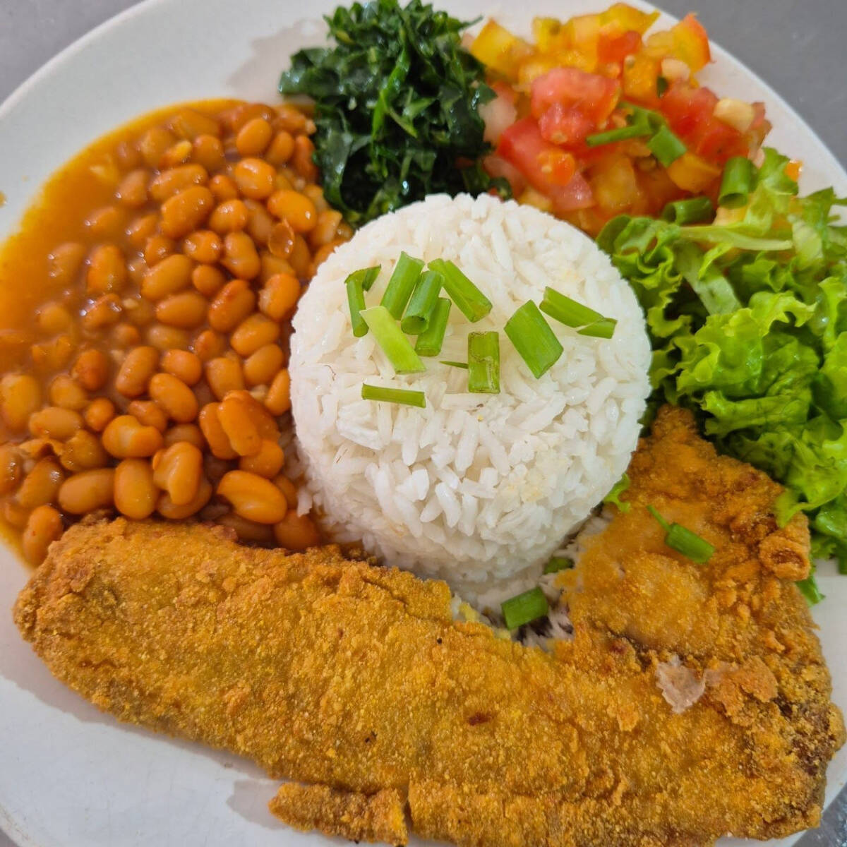 Arroz, feijão simples, batata frita tipo chips, peixe empanado, salada de alface e tomate.