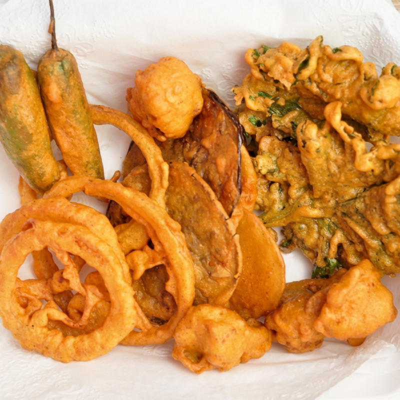 Batata e cebola co uma textura crocante. eles são empanados e fritos em farinha de grão de bico. acompanha chutney de hortelã e tâmara. 8-10 unidades Pakoda de pimenta opcional