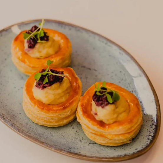 Massa folhada crocante recheada com brandade cremosa de bacalhau, batata e ervas, finalizado com tapenade de azeitonas.