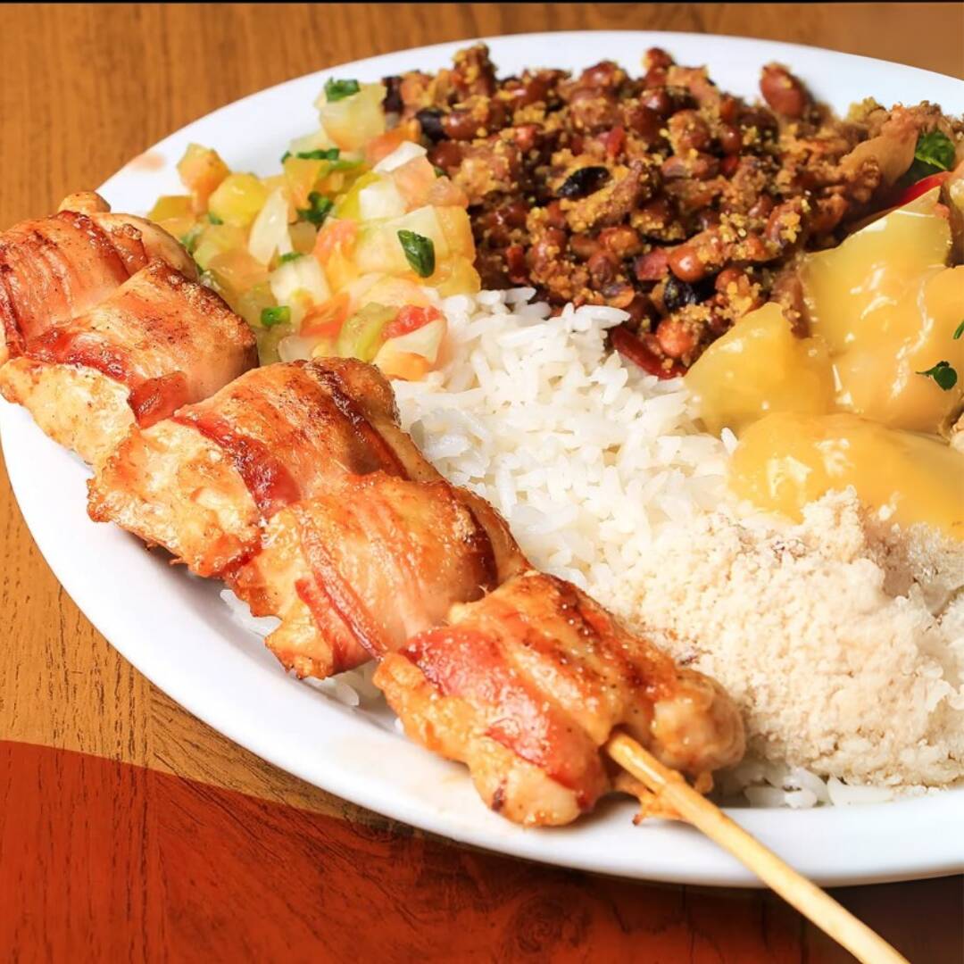 Marmita com Espetinho de frango grelhado + bacon com arroz soltinho, feijão tropeiro com banana frita, mandioca cozida e vinagrete fresco. Leve, completa e perfeita pro dia a dia. Serve 1 pessoa – Aproximadamente 650g.