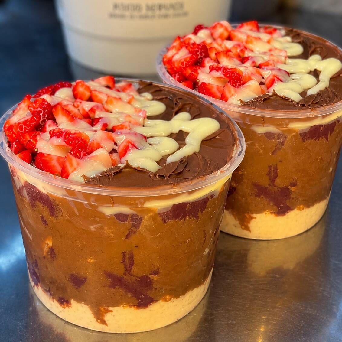 Dois potes com açaí artesanal trunfados com Nutella, leite em pó, choco power, morangos frescos e leite condensado .