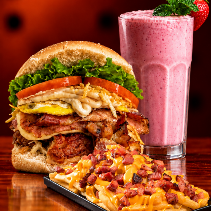 X-Tudo Burguer (pão com hambúrguer (100g), queijo, presunto, bacon, ovos, tomate, alface, milho e batata palha), acompanhado de Fritas com cheddar e bacon e 1 creme de morango 300ml. Uma combinação completa, com lanche reforçado, fritas caprichadas e um creme de morango para finalizar.