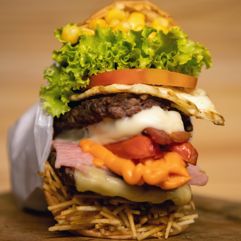 Carne Suculenta, Cheddar Cremoso, Ovo no Capricho, Milho Doce, Batata Palha Crocante, Alface e Tomate No Pão Macio Que Satisfaz!