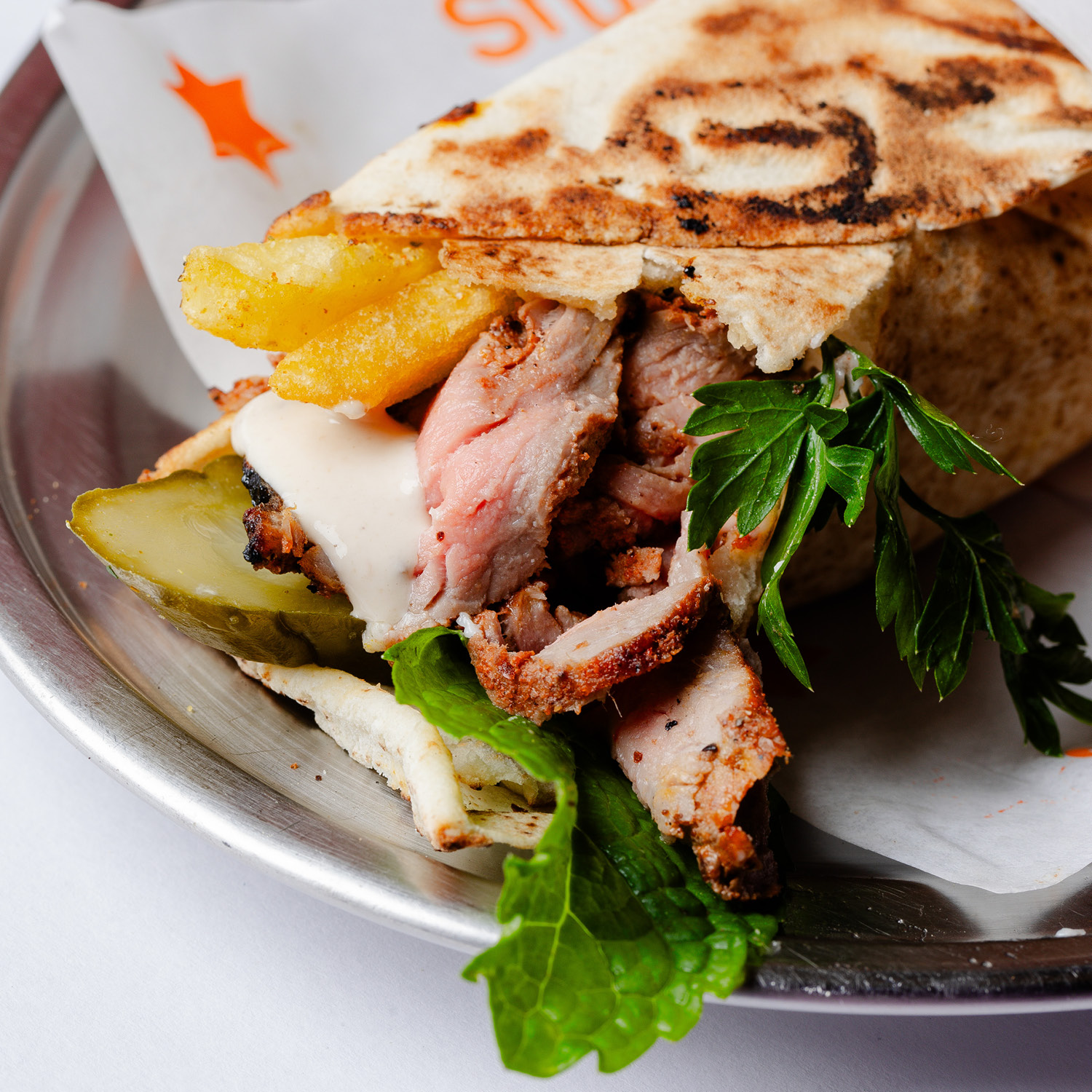 SANDUÍCHE ÁRABE DE CARNE COM ESPECIARIAS, PASTA DE ALHO, FRITAS (DENTRO DO LANCHE), SALSINHA FRESCA, VINAGRETE (TOMATE, CEBOLA E MELAÇO DE ROMÃ) E MOLHO TAHINE, ENROLADO NO PÃO SÍRIO E PRENSADO. CONTÉM GLÚTEN. CONTÉM LACTOSE. CONTÉM OLEAGINOSAS.
