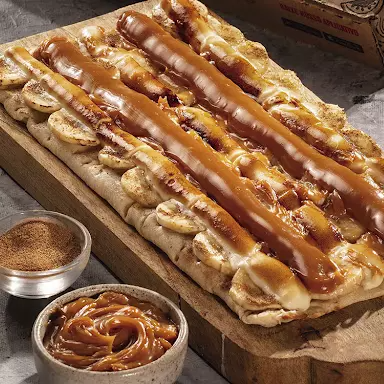 Banana fatiada, chocolate branco forneado crocante, doce de leite Santa Maria e finalizada com canela.