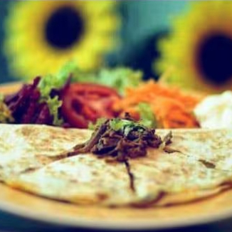 Tortilla de trigo em forma de pizza fechada, recheada com queijo derretido e tomate picado.