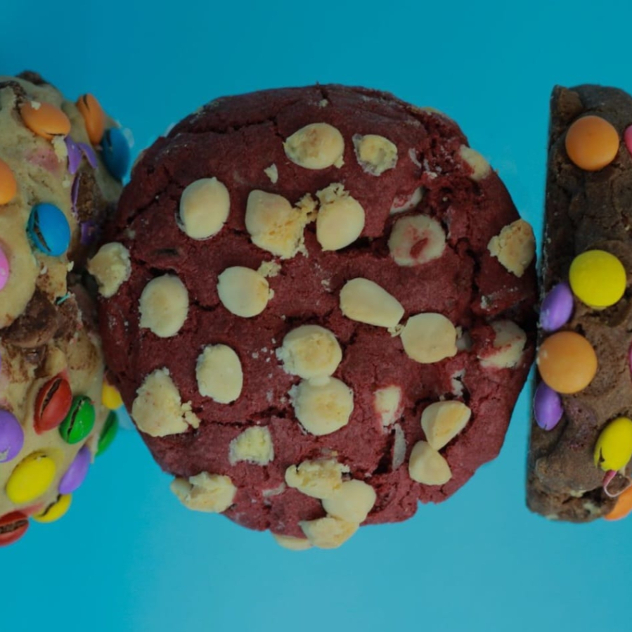 Cookie com massa de Chocolate, gotas de chocolate ao branco ou confetes e recheado com chocolate.Tem aproximadamente 65g