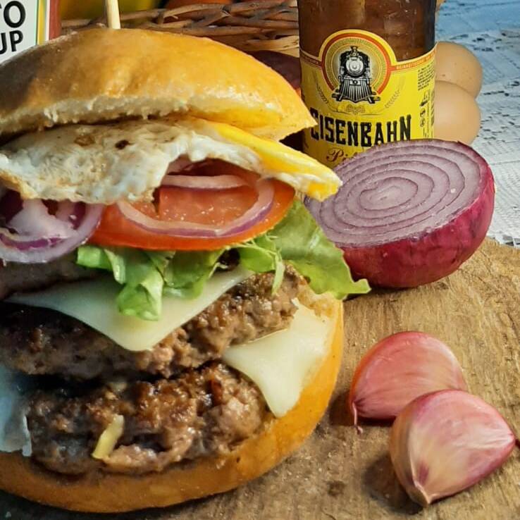 DOIS HAMBÚRGUERES ARTESANAIS DE 180 g, ACOMPANHADO COM QUEIJO CATUPIRY E MUSSARELA DERRETIDA, TIRAS DE BACON CROCANTE, OVO, SERVIDOS COM SALADA DE ALFACE, TOMATE E CEBOLA ROXA EM NOSSO DELICIOSO PÃO BRIOCHE PRODUZIDO NA CASA, E MAIONESE CASEIRA