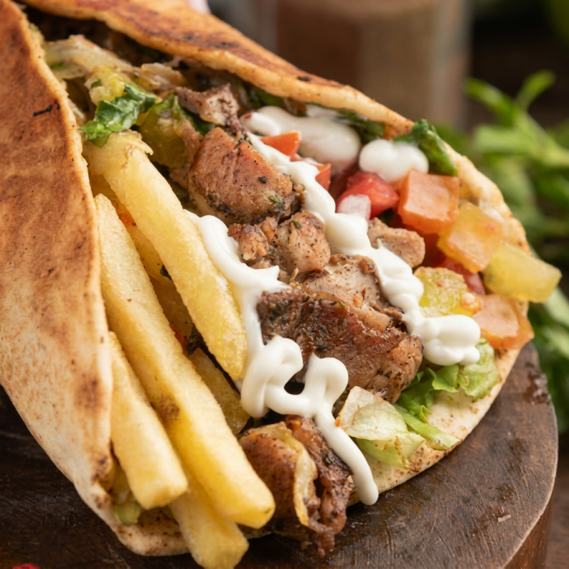 Descubra a sensacional experiência do nosso Shawarma, categoria 'Frango'. Este prato robusto é envolto em uma camada de pão sírio macio e leve. Em seu interior, encontra-se uma generosa porção de Frango suculento, meticulosamente temperada. Acompanha uma irresistível camada de creme de alho, que adiciona um sabor rico e cremoso. As batatas fritas crocantes inseridas dão um toque especial, enquanto os tomates frescos e a alface crocante proporcionam um saboroso contraste. Para completar, a cebola roxa acrescenta uma pitada de intensidade. Uma verdadeira explosão de sabores em cada mordida!
