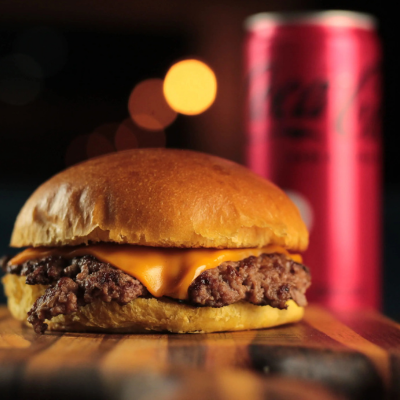 Hambúrguer Smash 100g Suculento com Cheddar Cremoso e Molho Especial da Casa, Acompanhado de Coca-Cola Bem Gelada 200ml.
