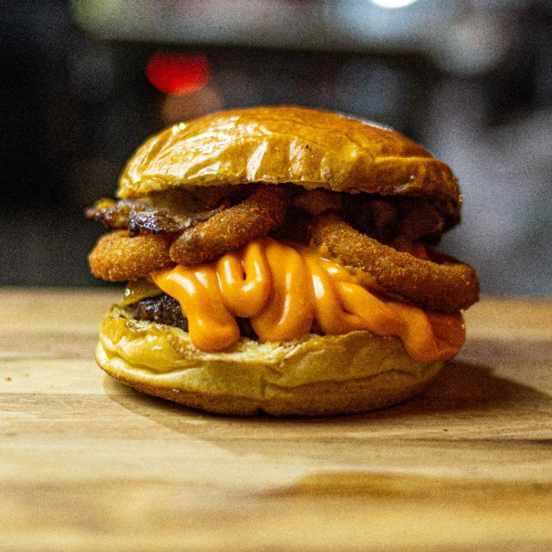 Pão brioche selado na brasa, blend 120g super suculento, bacon crocante, cheddar fatiado, cheddar cremoso, anéis de cebola e barbecue.