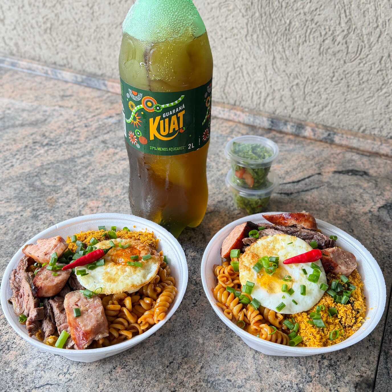 02 Marmitex de 750ml cada com Arroz branquinho, de feijão caldo, maionese de beterraba, macarrão ao molho da casa, ovo frito e Mix de churrasco com linguiça toscana de frango com bacon na brasa e saladinha separada fresquinha + 1 KUAT 2LT.