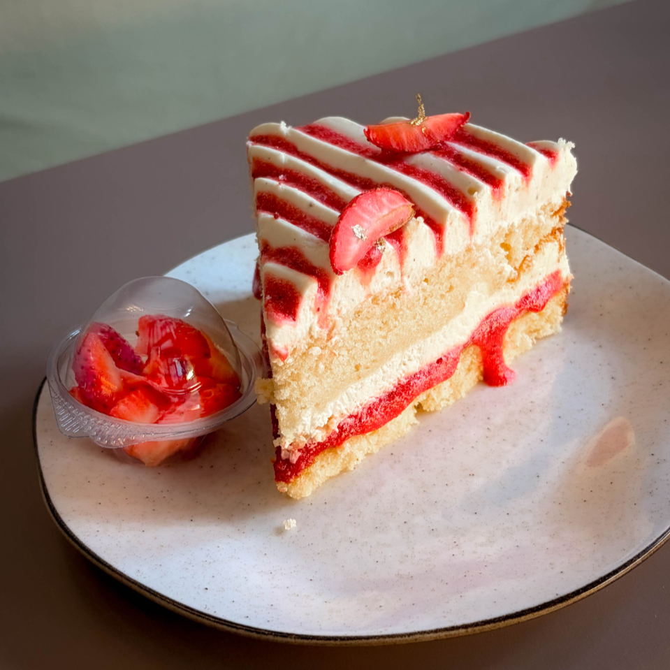 Fatia grande de bolo de morango com baunilha, preparada com massa leve e cremosa. Recheio e cobertura feitos com ganache de chocolate nobre branco e fava de baunilha natural. Entre as camadas, uma geleia de morango artesanal. Acompanha um potinho com morangos fatiados para colocar cima do bolo. Esse lançamento é ideal para quem adora morango e quer doce leve e refinado.