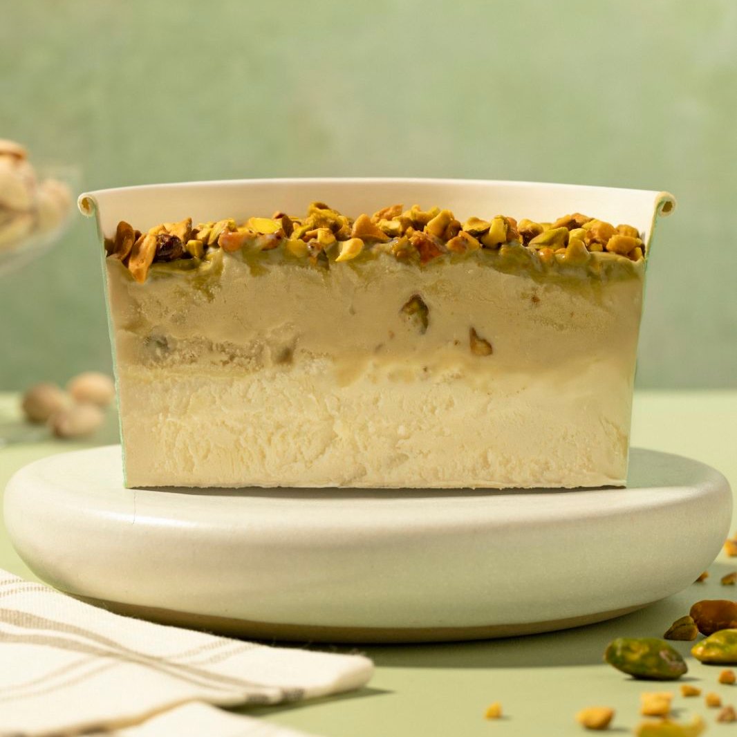 Camadas de gelato Bacio di Latte, recheio de chocolate branco, gelato de pistache, com calda de pistache crocante e pistaches torrados 1L.