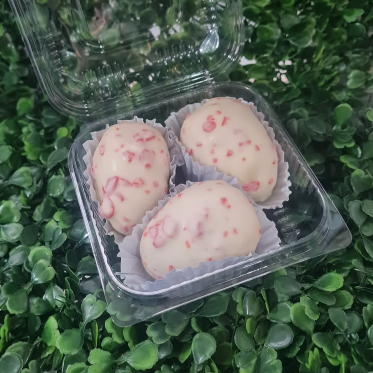 Três doces feitos com *** PEQUENOS *** morangos frescos cobertos por brigadeiro branco, chocolate branco e pedaços crocantes de caramelo vermelho. Sua aparência lembra a de uma joia cravejada.