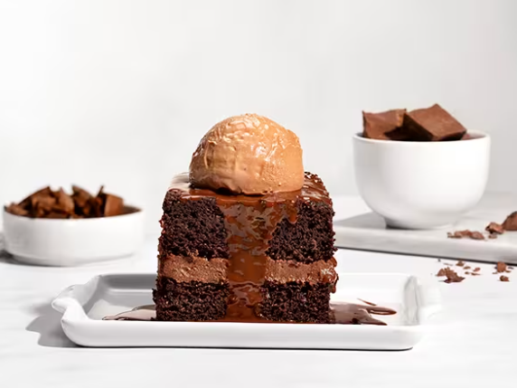 Uma fatia de bolo de chocolate, recheado com ganache de chocolate meio amargo, coberto por calda de chocolate, finalizada com a nossa mousse de chocolate cremoso.