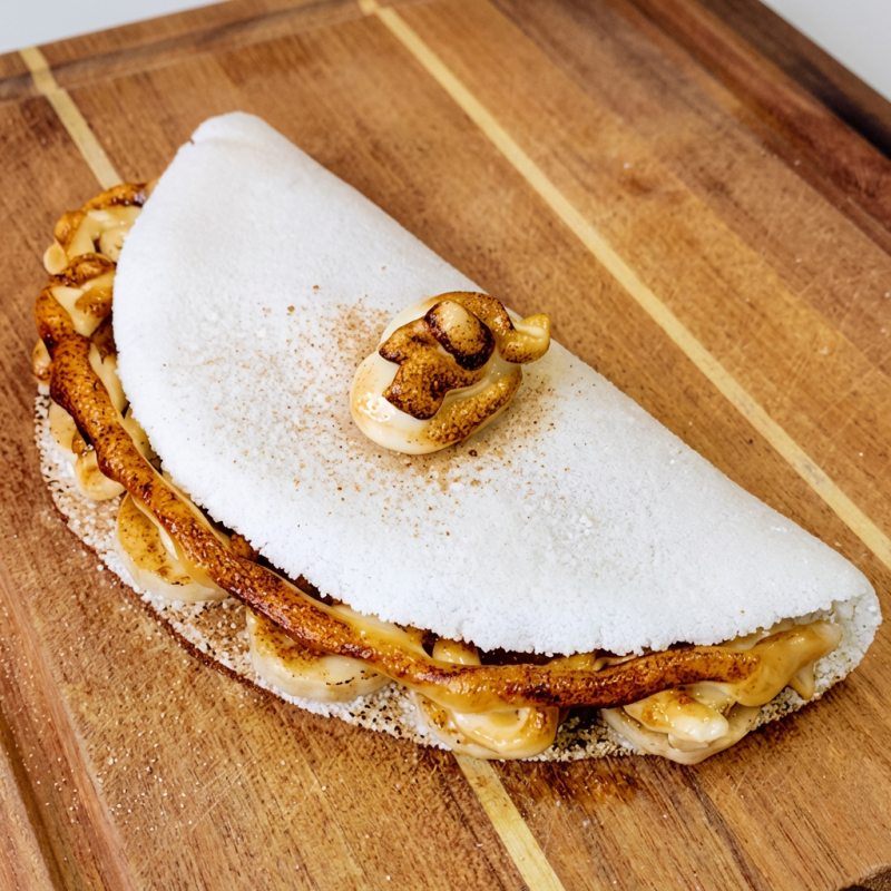 Apresentamos a 'Banana Nevada 2.0', porque quem disse que pizza e tapioca não podem se unir em uma combinação épica? Imagine fatias de banana dançando em harmonia com a cremosidade da mussarela, os aromas tentadores da canela e a doçura do açúcar, tudo coberto por uma camada de doce de leite e chocolate branco flambados. Esta é uma experiência que redefine o conceito de delícia. Simplesmente irresistível!