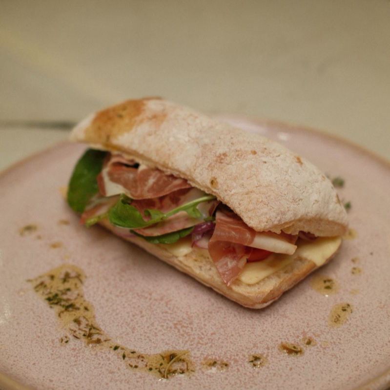 Pão ciabatta crocrante, muçarela, presunto serrano, rúcula, tomate cereja e cebola roxa.