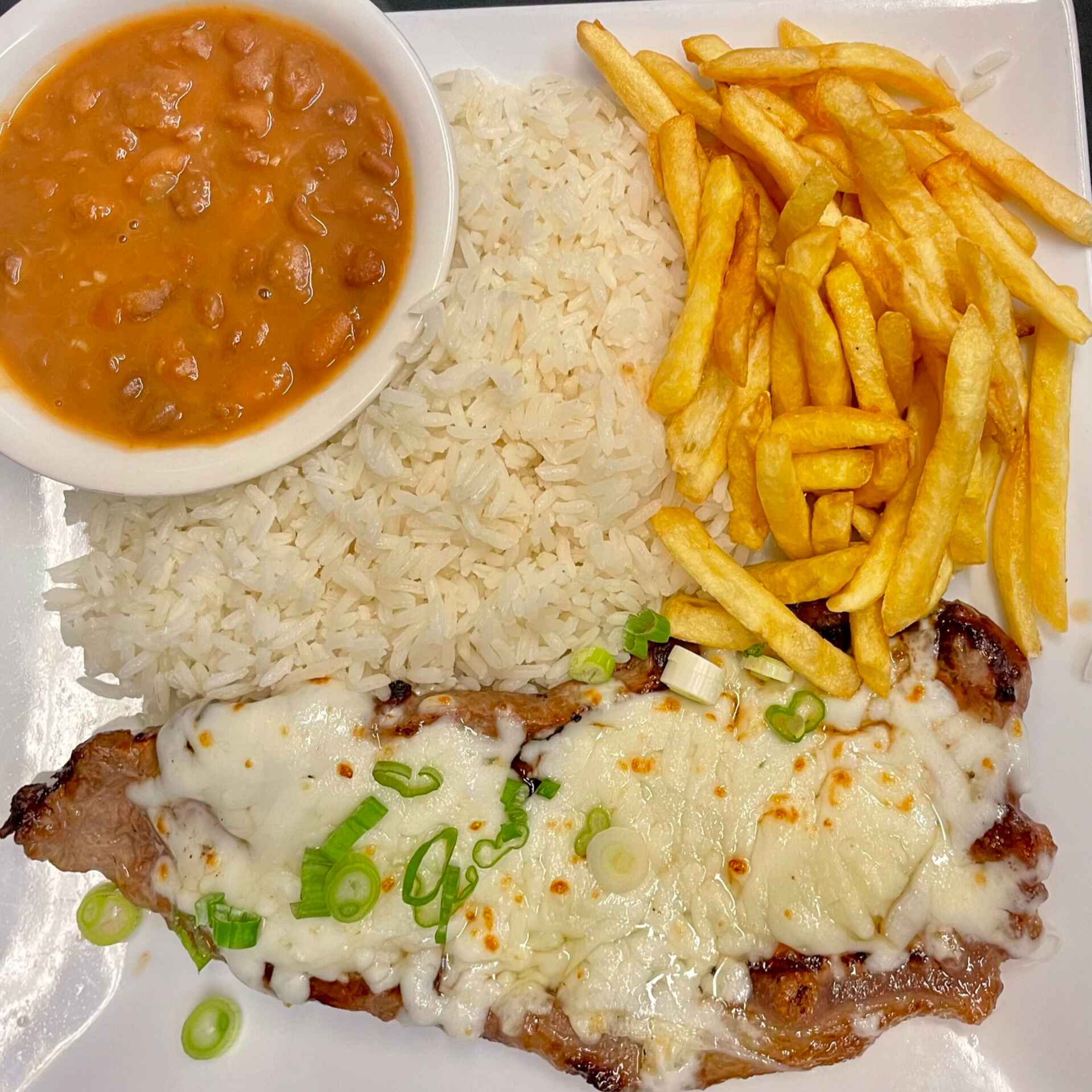 Arroz soltinho, feijão com caldinho e um bife generoso de contra-filé com fatias de queijo derretido e fritas crocantes