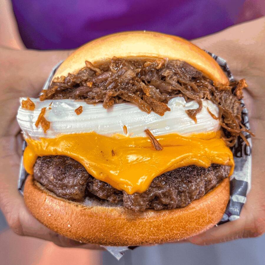 O Cometa Halley é uma verdadeira explosão de sabores robustos, servido em nosso pão brioche premium, reconhecido por ser extremamente amanteigado, macio e selado com perfeição. O hambúrguer de 150g, extremamente suculento, é elevado a outro nível com uma fatia generosa de queijo cheddar derretido e uma camada generosa de cream cheese cremoso. A experiência se torna única com a adição da nossa costela desfiada artesanal ao molho barbecue e a finalização com cebola crocante (crispy), que traz a crocância ideal para contrastar com a maciez do pão e a cremosidade dos queijos.