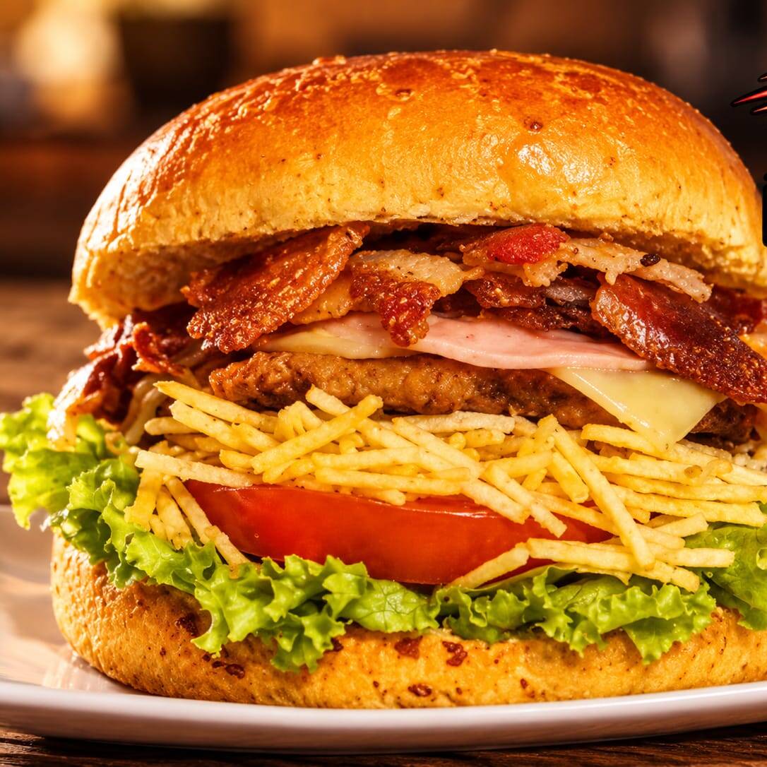 Hambúrguer suculento com bacon crocante, presunto e queijo derretido, acompanhado de batata palha crocante, milho, alface fresca e tomate. Finalizado com ketchup e maionese para entregar uma combinação farta, cremosa e cheia de sabor.
foto ilustrativa