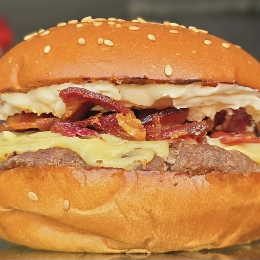Burguer fininho de 100g, (fake smash) feito no charbroiler, 2 fatias de queijo prato top, bacon crocante e sequinho em pedaços, molho the best suculento em um pão brioche artesanal com gergilin com gergilim bem fofinho. OBS: não alteramos o queijo e nem o ponto da carne.