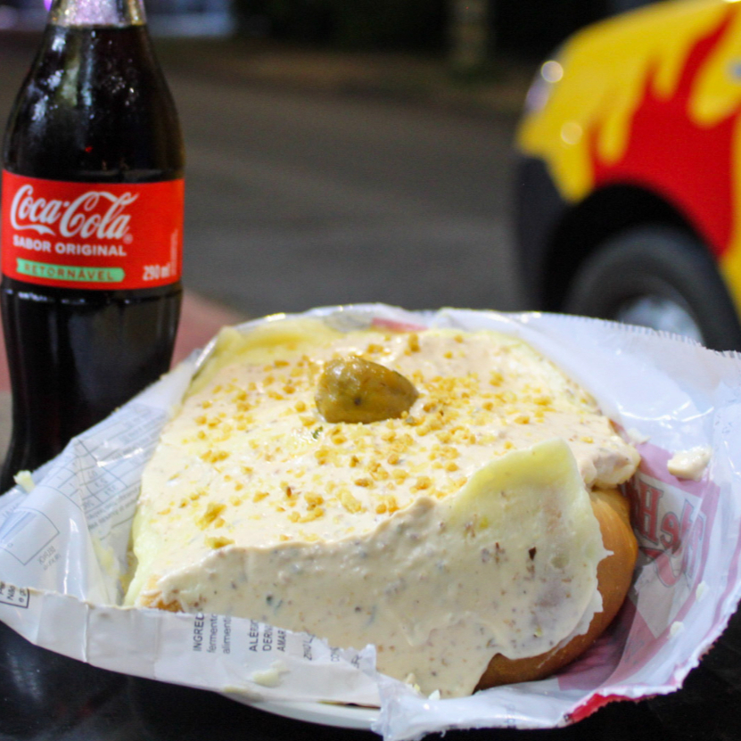 Pão, salsicha, ketchup e mostarda, vinagrete sem cebolas, milho, batata palha, purê de batatas maravilhoso, Maionese hellmans temperada com pate de azeitonas pretas, Bacon em Cubos e Chimicurry, alho frito e uma azeitona.