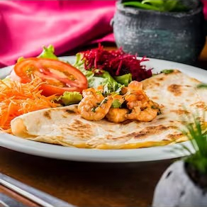 Tortilla de trigo em forma de pizza fechada, recheada com queijo derretido e tomate picado.