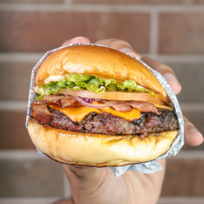 Pão brioche selado na manteiga, com um suculento blend bovino de 150g, queijo cheddar, tomate, cebola roxa, alface, bacon e molho Mac.