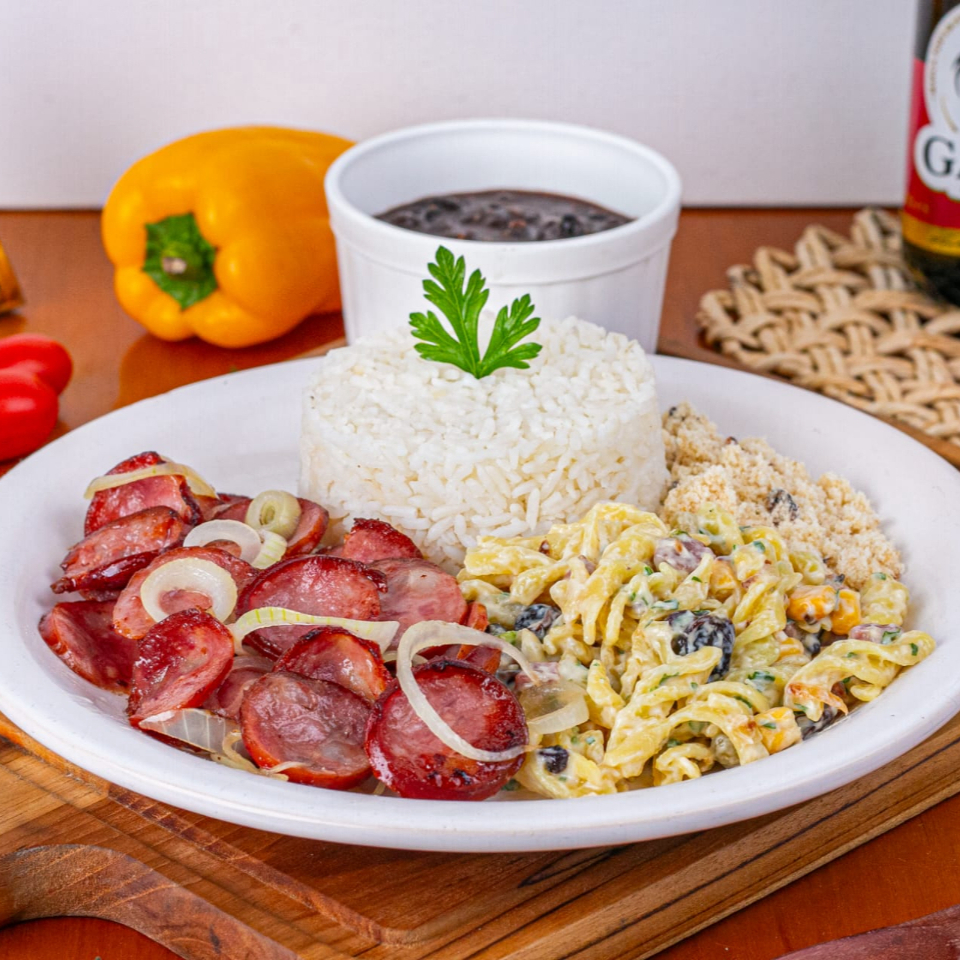 Linguiça Calabresa Acebolada Com Macarronese, acompanhado por um arroz branco soltinho, um feijão caseiro repleto de sabor, farofa crocante. Todos esses itens são servidos em uma prática marmita com aproximadamente 600gr, nossa embalagem vai ao microondas.