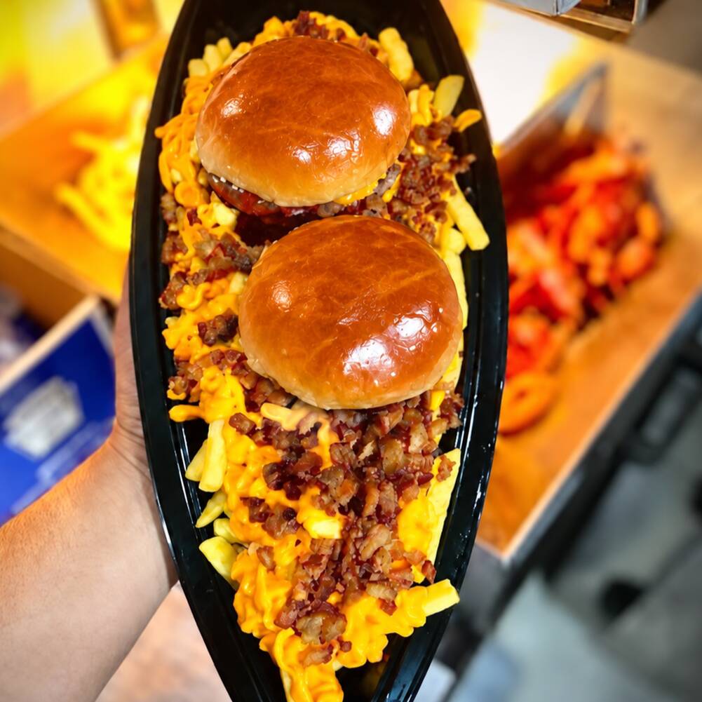 2 Burguers (pão brioche com burguer bovino(100g), salsicha, ovo e cheddar), acompanhados de fritas com cheddar cremoso e bacon crocante. Uma barca generosa e bem recheada.