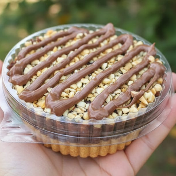 Tortinha com base de farofa de biscoito maisena tritirada, creme de chocolate, amendoim triturado e riscos de Nutella. Aproximadamente 120g. Serve 1 pessoa.