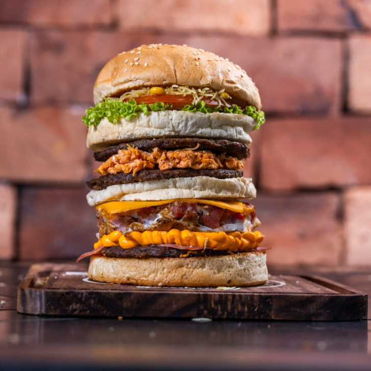 Pão artesanal, 3 suculentas carnes bovina, ovo gema firme, bacon em cubos, queijo prato derretido, presunto, frango desfiado, Catupiry ou Cheddar, milho verde, batata palha fina, alface crespa e tomate fresco