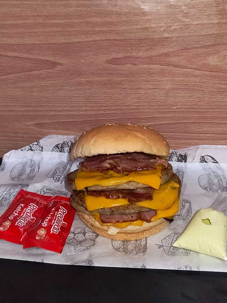 pão , 3 carnes , 3 fatias de queijo cheddar , 3 bacons , ketchup e molho verde