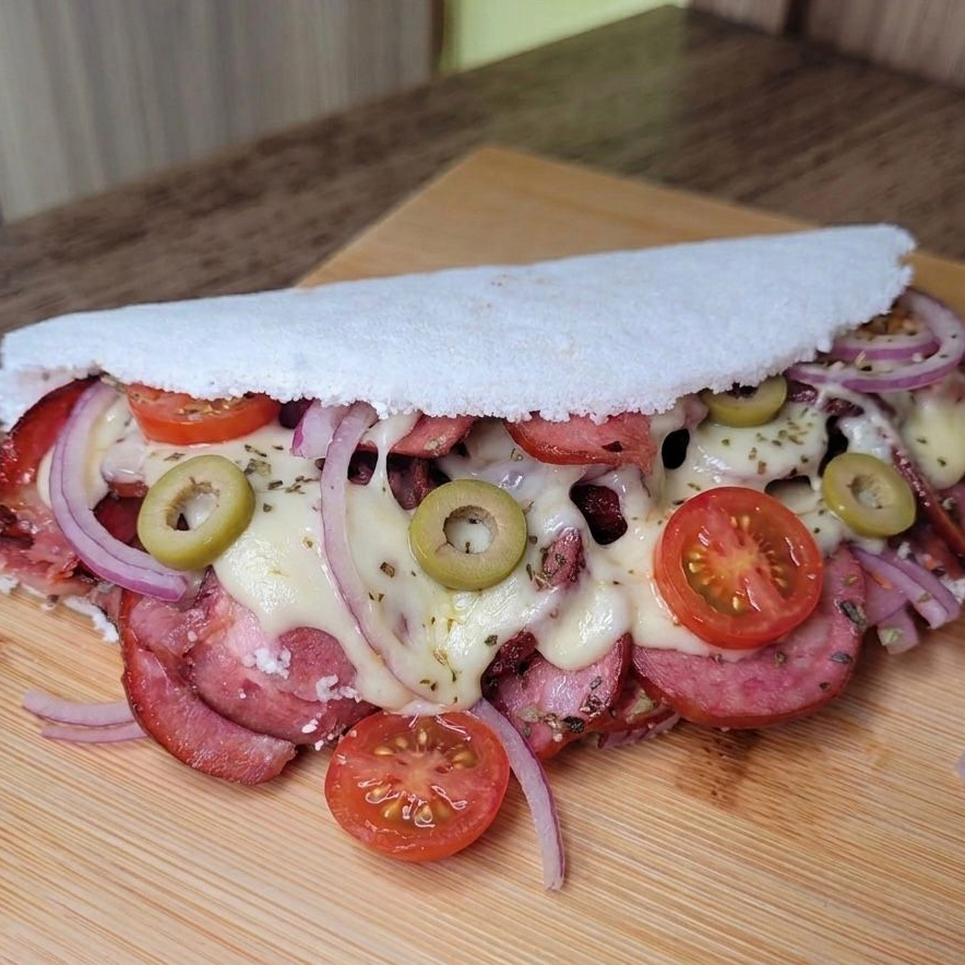 Goma de tapioca artesanal, calabresa fatiada, rodelas de tomate frescas, cebola roxa e azeitonas verdes, queijo derretido finalizada com um toque de orégano.